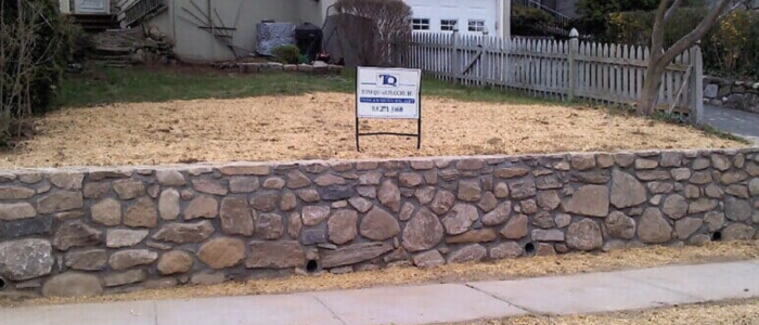 A stone wall with a Tom Quartuccio Jr, LLC sign atop it