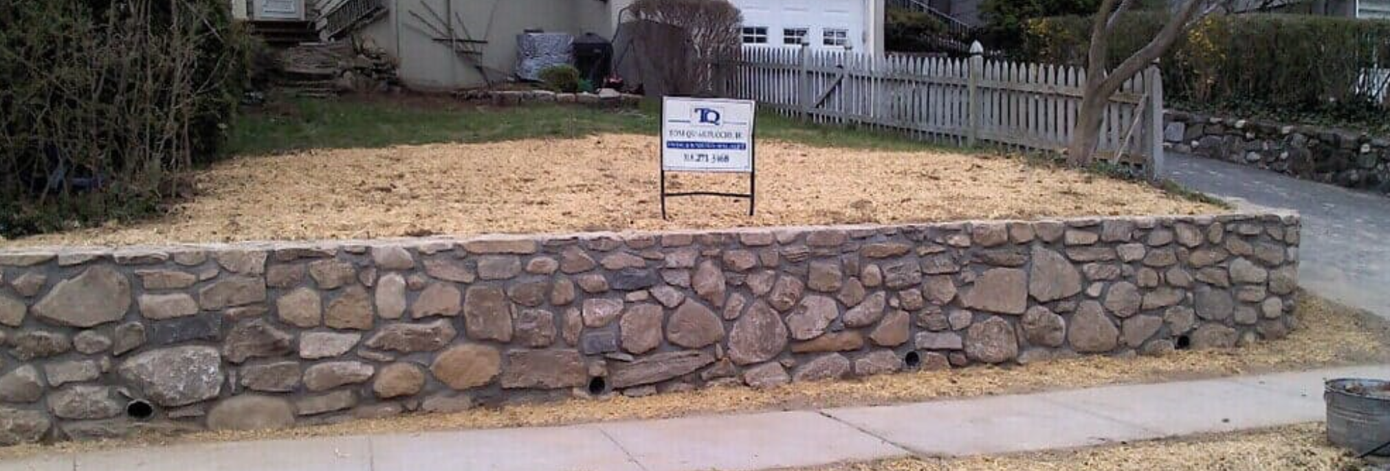 A stone wall with a Tom Quartuccio Jr, LLC sign atop it