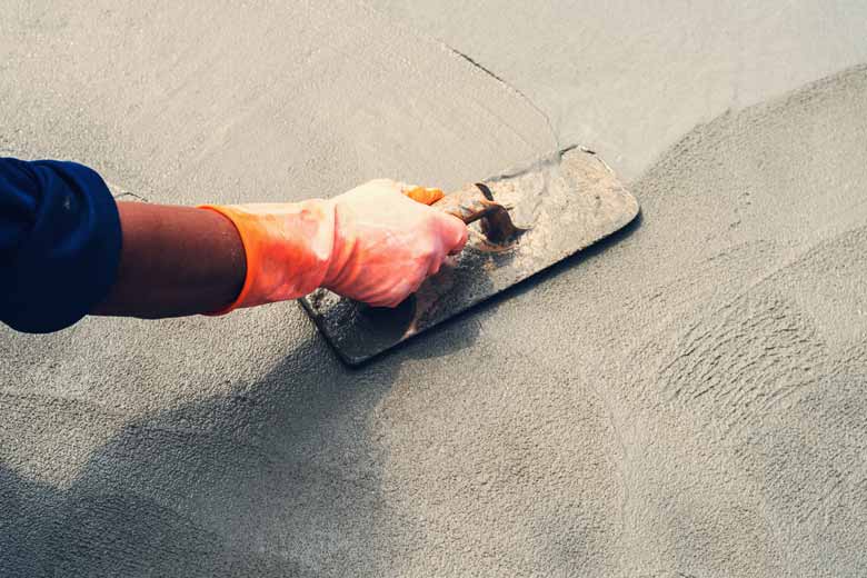 A hand wearing an orange glove smoothing over wet concrete