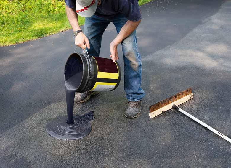 A man applying a top coat of sealant to an asphalt driveway