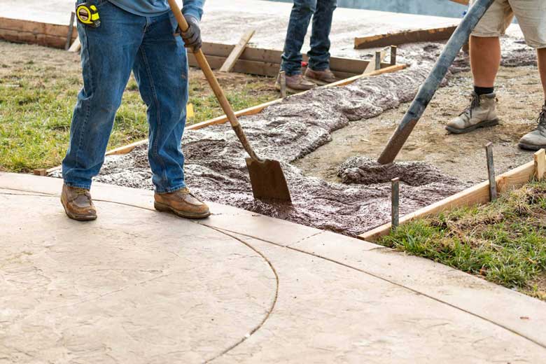 A crew of workers pouring concrete to create a walkway up to a concrete patio